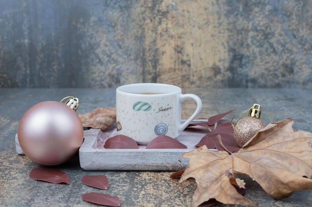 Bola grande de Navidad con taza de té sobre tabla de madera.