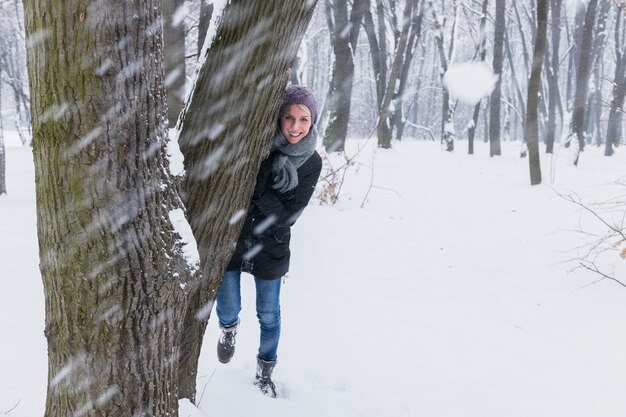 Bola de nieve frente a la mujer sonriente de pie detrás del árbol