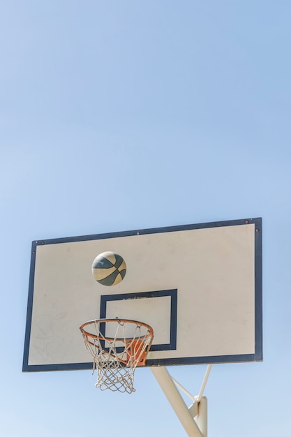 Bola que cae en el aro de baloncesto contra el cielo claro