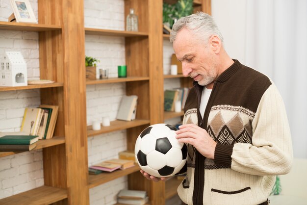 Bola que se sostiene masculina envejecida cerca de los estantes en sitio