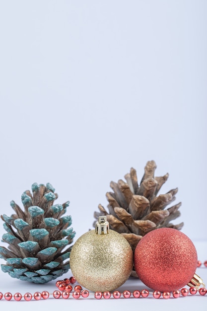 Bolas de árbol de Navidad y conos de roble con cadena de perlas rojas sobre el blanco