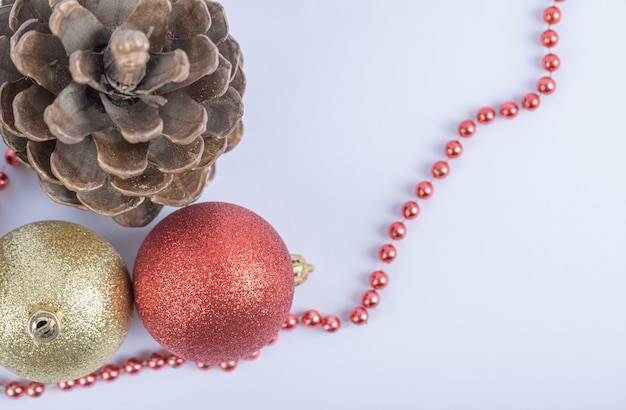 Bolas de árbol de navidad y conos de roble con cadena de perlas rojas sobre el blanco