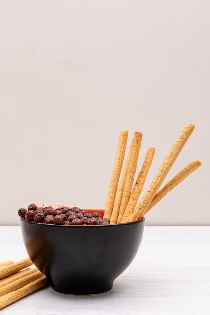 Bolas de cereales con palitos de pan en un tazón sobre superficie blanca