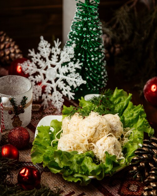 Bolas de ensalada cubiertas de queso rallado servidas en un recipiente decorado con lechuga