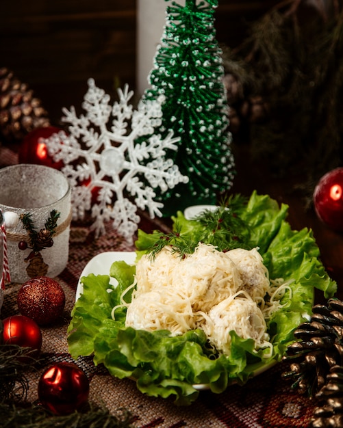 Bolas de ensalada cubiertas de queso rallado servidas en un recipiente decorado con lechuga