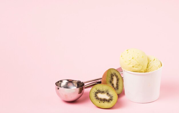 Bolas de helado en taza cerca de kiwi y cuchara