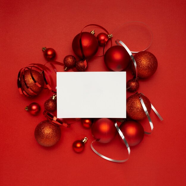 Bolas de Navidad rojas y tarjeta en blanco sobre mesa roja