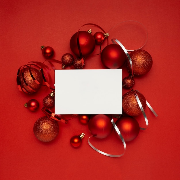 Bolas de Navidad rojas y tarjeta en blanco sobre mesa roja