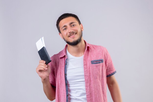 Boletos de avión de chico joven guapo viajero mirando a la cámara con sonrisa de confianza en la cara feliz y positivo de pie sobre fondo blanco