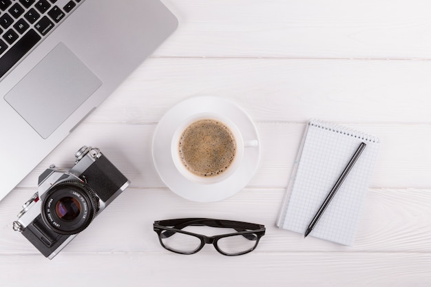 Foto gratuita bolígrafos cerca de bloc de notas, cámara, gafas, taza y portátil