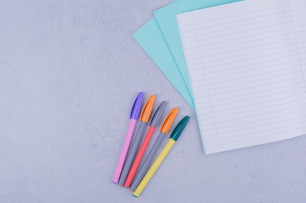 Bolígrafos multicolores y un trozo de papel en blanco a cuadros.