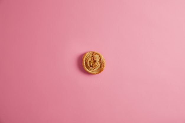 Bollo espiral recién horneado en casa para su delicioso desayuno para satisfacer los golosos. Apetitosa y deliciosa pastelería con muchas calorías, fotografiada desde arriba sobre fondo rosa. Postre aromático