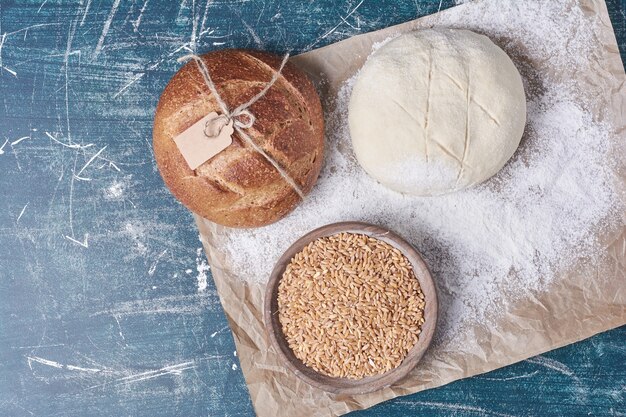 Bollo de pan con masa y trigo en mesa azul.