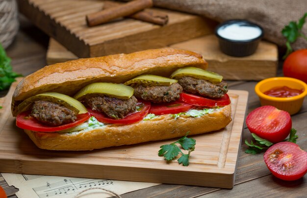 Un bollo de pan relleno de albóndigas, pimiento verde, rodajas de tomate y salsa de bocadillo