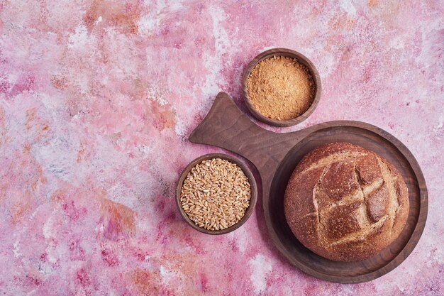 Bollo de pan y trigo mezclado en mesa rosa.