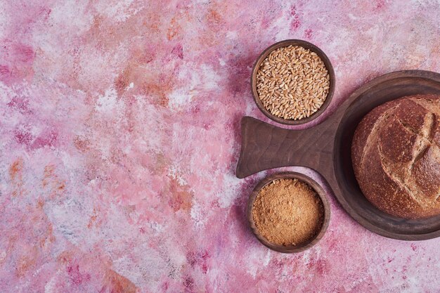 Bollo de pan y trigo mezclado en mesa rosa.