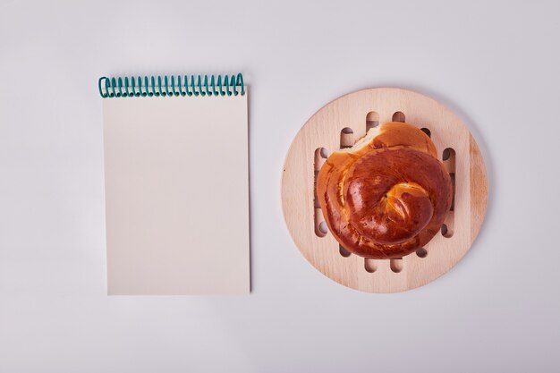 Bollo de pastelería de estilo caucásico en bandeja de madera con un libro de recetas a un lado.