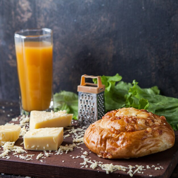 bollo con queso y jugo de naranja y rallador en tablón de madera