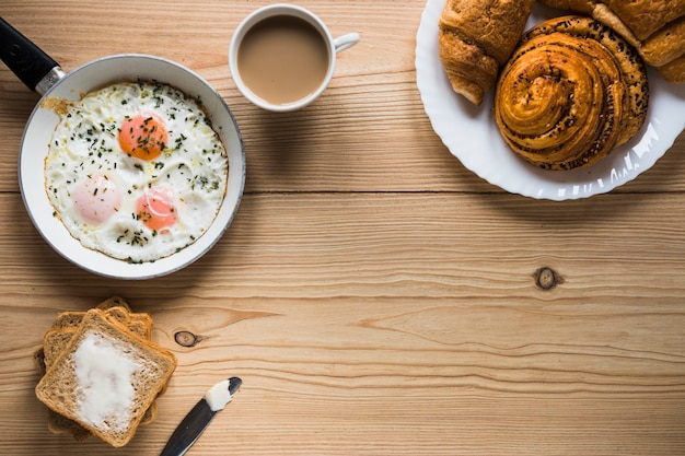 Foto gratuita bollos y café cerca de huevos fritos y tostadas