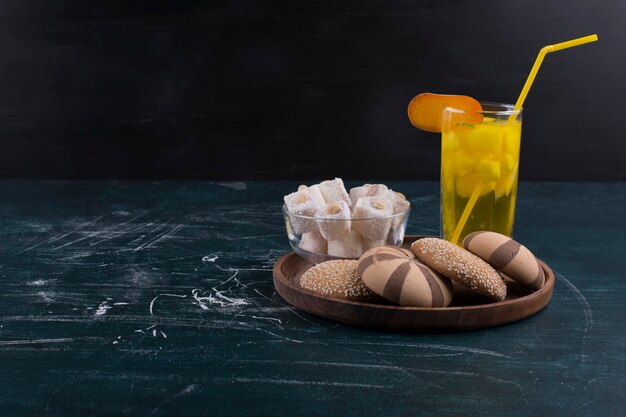 Bollos de galleta de cacao y vainilla con lokum y un vaso de jugo en bandeja de madera