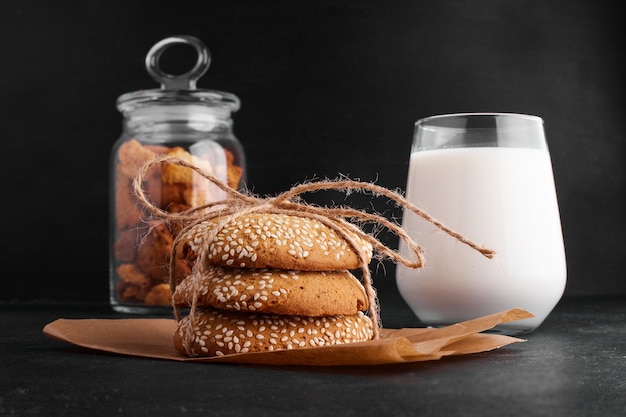 Bollos de galleta de sésamo sobre papel servido con un vaso de leche.