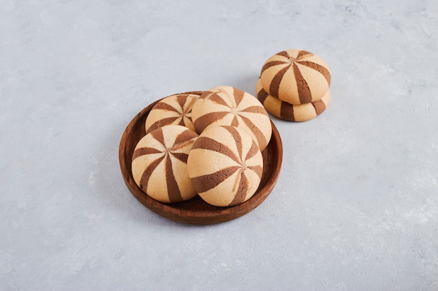 Bollos de galleta de vainilla y cacao en un plato de madera sobre una superficie blanca, vista superior.