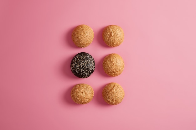 Bollos de hamburguesa fresca con semillas de sésamo dispuestas en dos filas sobre un fondo rosado. Preparación de comida rápida o hamburguesa casera. Fotografía gastronómica. Alimentación o dieta poco saludables. Brioches suaves redondos. Enfoque selectivo