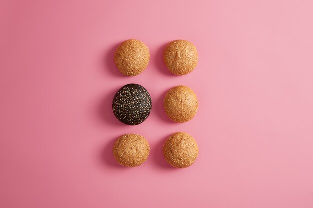 Bollos de hamburguesa fresca con semillas de sésamo dispuestas en dos filas sobre un fondo rosado. Preparación de comida rápida o hamburguesa casera. Fotografía gastronómica. Alimentación o dieta poco saludables. Brioches suaves redondos. Enfoque selectivo