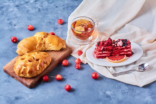 Bollos con pastel de terciopelo rojo y té sobre una tabla de madera en azul