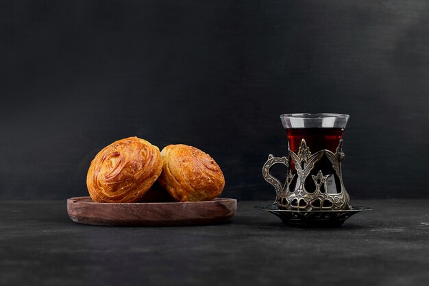 Bollos de repostería con un vaso de té sobre fondo negro. Foto de alta calidad