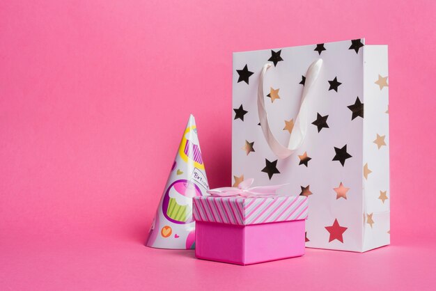 Bolsa de compras en forma de estrella; sombrero de papel y caja de regalo en fondo rosa