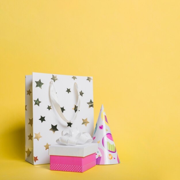 Bolsa de compras en forma de estrella; sombrero de papel y caja de regalo sobre fondo amarillo