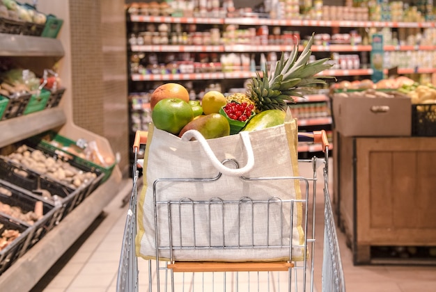 Bolsa ecológica con diferentes frutas y verduras en un carrito de compras.