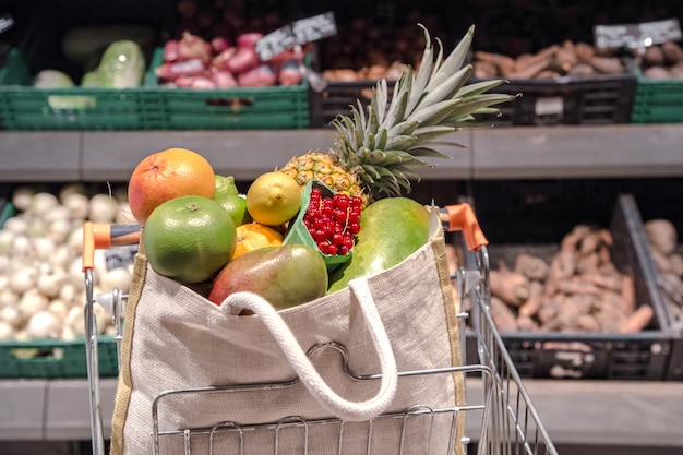 Bolsa ecológica con diferentes frutas y verduras en un carrito de compras.