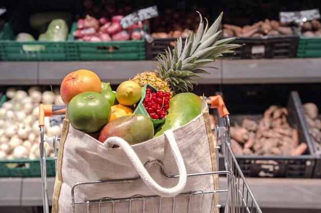 Bolsa ecológica con diferentes frutas y verduras en un carrito de compras.