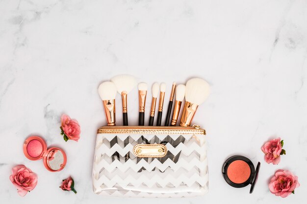 Bolsa de maquillaje blanca con pinceles; polvo compacto y rosas sobre fondo texturizado