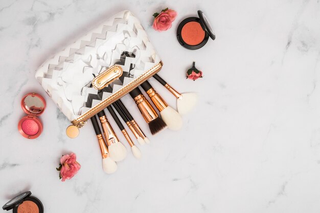 Bolsa de maquillaje profesional con pinceles y polvo compacto sobre fondo de mármol.