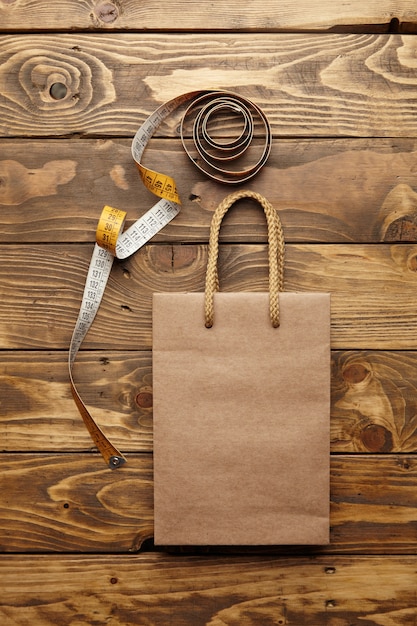 Foto gratuita bolsa marrón para llevar de papel artesanal reciclado thic sobre una mesa de madera rústica cerca del medidor de sastrería vintage desenrollado