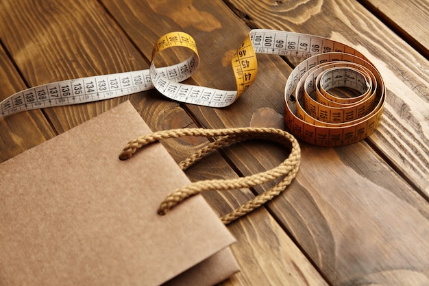 Foto gratuita bolsa marrón para llevar de papel artesanal reciclado thic sobre una mesa de madera rústica cerca del medidor de sastrería vintage vista cercana