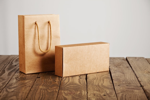 Bolsa de papel artesanal y caja de cartón en blanco presentada en mesa de madera rústica, aislado sobre fondo blanco.