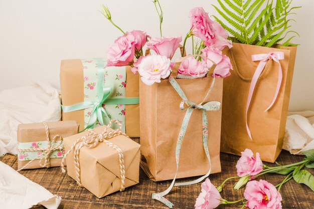 Bolsa de papel llena de flores frescas y regalo envuelto sobre superficie de madera