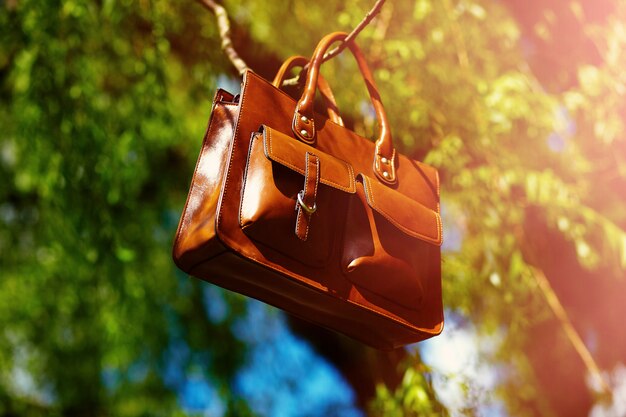 Bolso de cuero retro hombre marrón en el parque de verano colorido brillante colgando de leafes