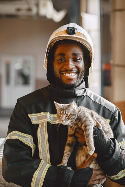 Bombero de Arfican en uniforme. El hombre se prepara para trabajar. Chico con gatito.