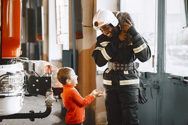 Foto gratuita bombero de arfican en uniforme. el hombre se prepara para trabajar. chico con niño.