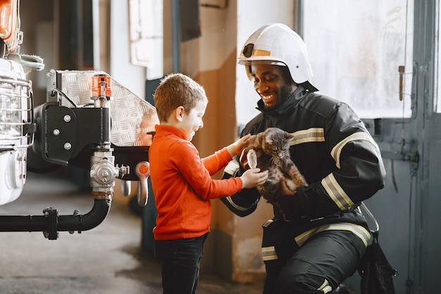 Bombero de Arfican en uniforme. El hombre se prepara para trabajar. Chico con niño.