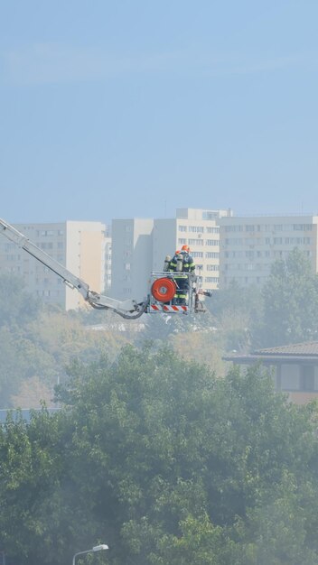 Bomberos en un camión de plataforma que va al techo de una casa en llamas. Vista de los bomberos tratando de extinguir el fuego del edificio en llamas y humos. Hombres que detienen el smog y el humo de la casa.