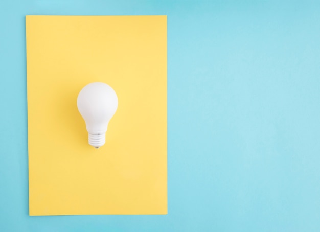 Bombilla de luz blanca en papel amarillo sobre el fondo azul