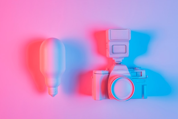 Bombilla de luz rosa y cámara con luz azul sobre superficie rosa