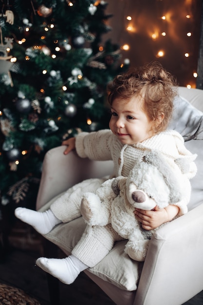 Bonita chica caucásica con cabello rizado se sienta cerca de un gran árbol de Navidad hermoso y se relaja