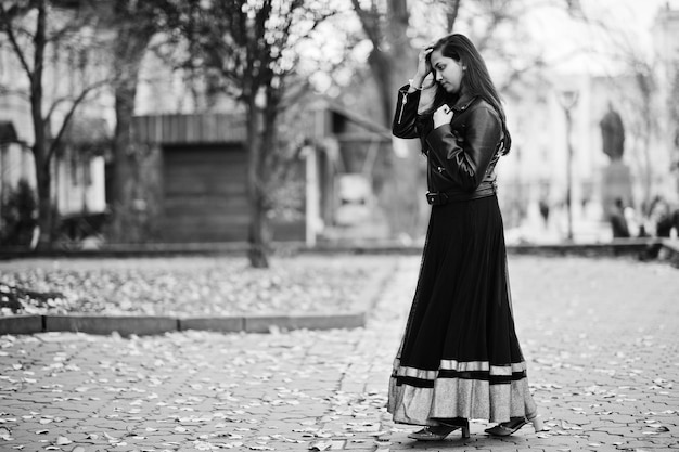 Bonita chica india con vestido de sari negro y chaqueta de cuero posada al aire libre en la calle de otoño